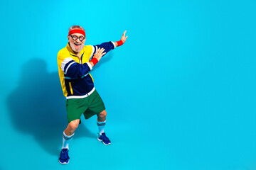 Obraz premium Energetic senior man in retro workout outfit celebrating fitness and fun with a playful pose against a bright blue background