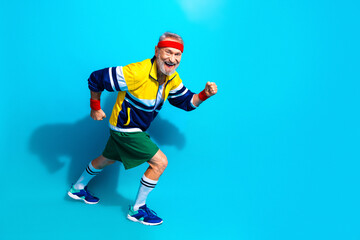 Obraz premium Happy senior man jogging in retro sportswear on blue background — active fitness lifestyle for elderly and mature adults