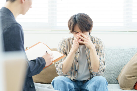 ソファに座ってカウンセリングを受ける若い日本人男性