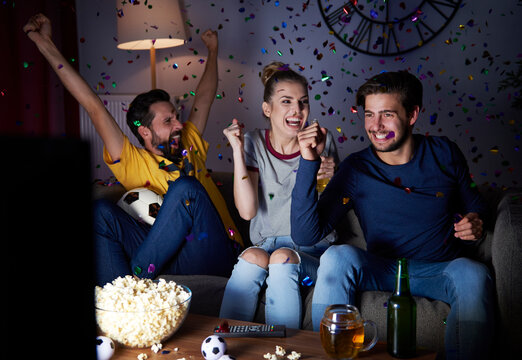 Excited friends sitting on the sofa watching Tv