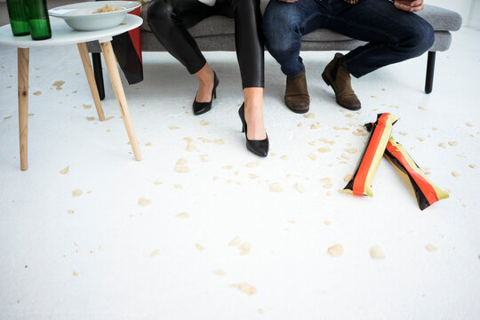 Legs of German football fans sitting on couch with chips scattered on the floor
