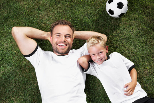 Germany, Father and sun lying on lawn, wearing football shirts