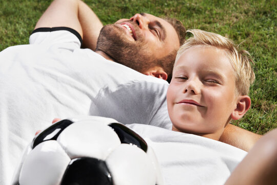 Germany, Father and sun lying on lawn, wearing football shirts