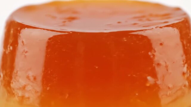 Macro shot of glossy orange jelly dessert or fruit confectionery against white background, highlighting smooth texture and vibrant color
