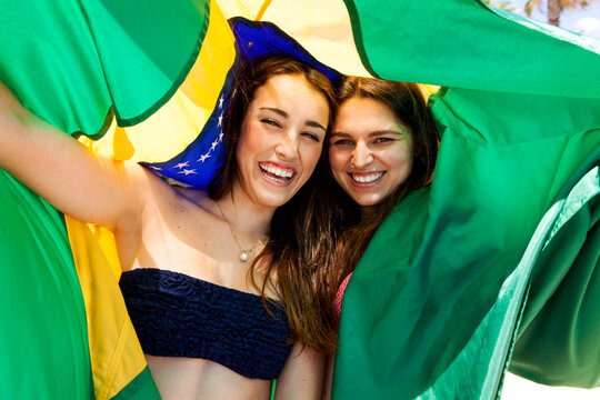 Two friends wearing beachwear playing with Brazilian flag
