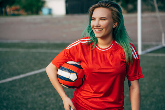 Smiling young woman standing on football ground holding the ball