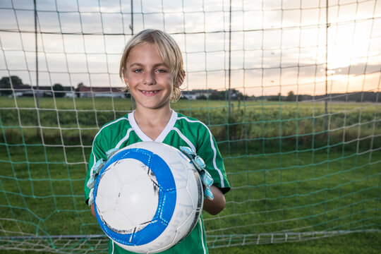 Portrait of smiling young football goalkeeper holding ball on football ground