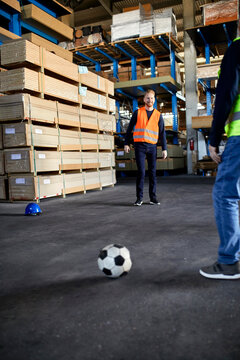 Workers playing football in factory warehouse