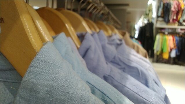 Row of light blue and purple shirts on wooden hangers in a store.