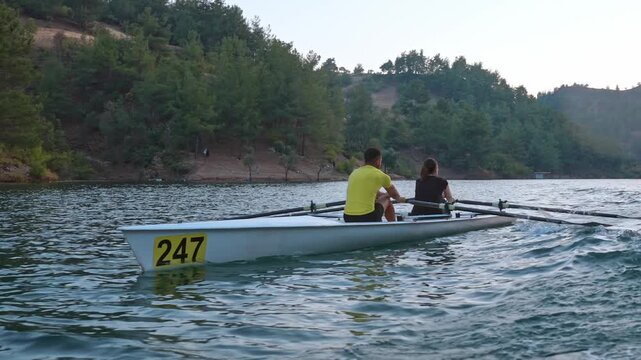 Close-up shot of two rowers moving across a calm lake in a double scull. Outdoor water sports scene with motion, teamwork, freshwater and active lifestyle atmosphere.