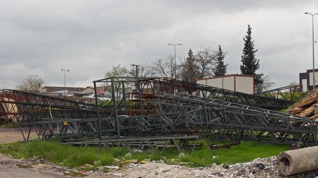 Cinematic 4K footage of a large collapsed steel truss structure piled on a roadside with debris and litter nearby. Urban decay, disaster aftermath or demolition concept. Overcast sky.