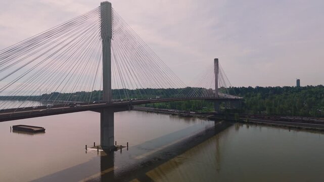 Port Mann Bridge cable architecture stretching across wide muddy river water carrying heavy commuter traffic past industrial floating wood barge reflecting massive concrete pillars below hazy bright