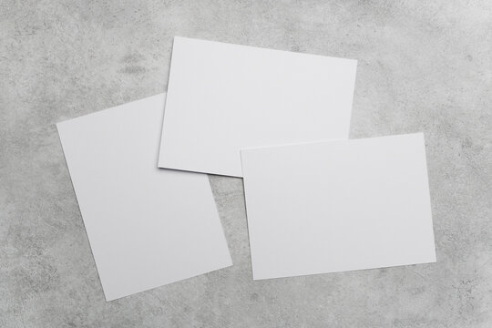Three blank white sheets of paper with copy space, arranged on a textured gray concrete surface, showcasing a clean and minimalistic design for various creative applications