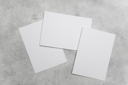 Three blank white paper cards arranged on a textured gray concrete surface, showcasing a clean and minimalist design suitable for various creative projects, copy space for design presentation