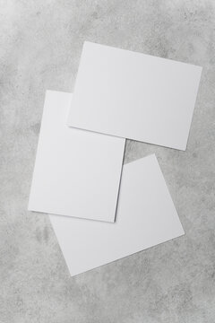 Three blank white sheets of paper arranged at different angles on a textured gray concrete surface, suitable for design mockups or presentations