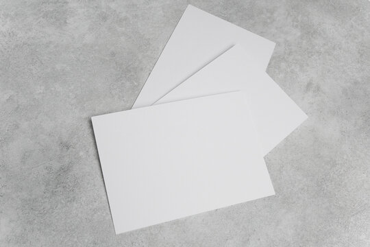 Three blank white cards arranged on a textured gray concrete surface, ideal for design mockups or presentations with ample space for text and graphics