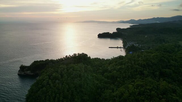 Aerial orbit of Virac, Catanduanes, Philippines showing a forested coastline, calm bay, and tropical shoreline under sunset light