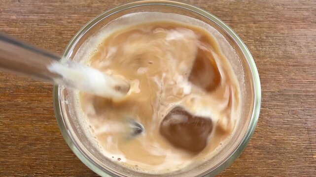 Stirring ice cold latte coffee with glass straw and ice cubes close up