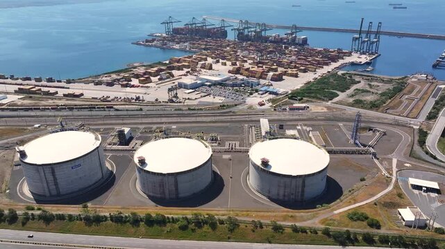 LNG terminal with gas storage tanks located on the coastline near a port. Cargo ships are present in the background, supporting energy supply in the European market.