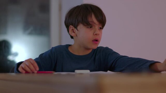 Young boy sitting at table during homework session rubbing face with bored expression while pencil and worksheet rest in front of him