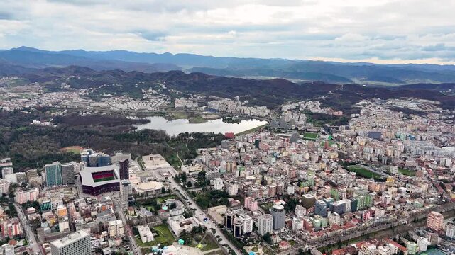 Aerial camera flies forward high over Tirana, Albania, pushing toward the Grand Park lake with Air Albania Stadium and Mother Teresa Square visible below against rolling mountains