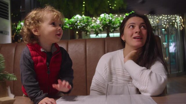Mother and toddler sitting at restaurant booth sharing playful conversation during family dinner expressing bonding warmth and everyday parenting moment