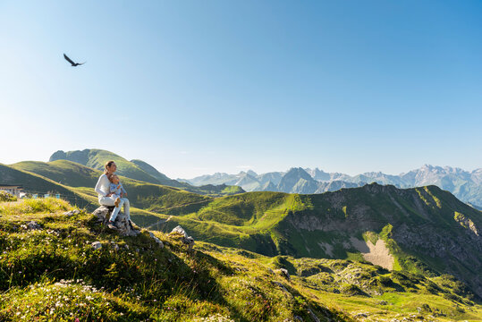 Germany, Bavaria, Oberstdorf, mother and little daughter on a hike in the mountains having a break looking at view
