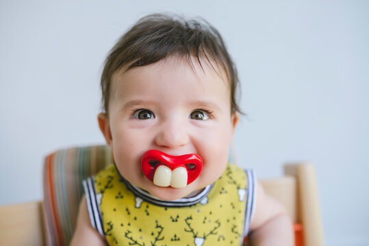 Portrait of baby girl sucking a pacifier with false teeth and mouth