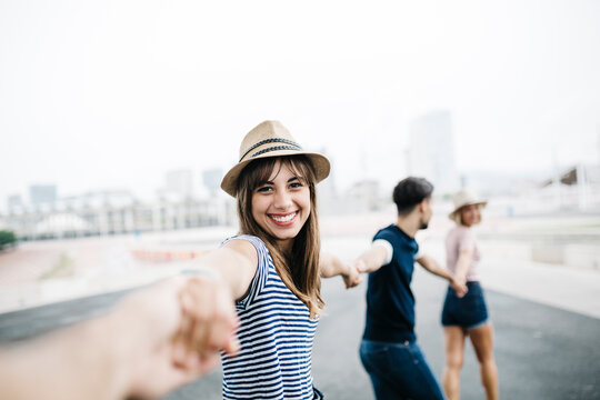 Spain, Barcelona, portrait of smiling young woman holding hands with her friends