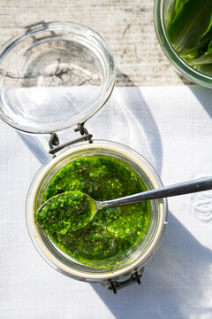 Preserving jar of wild garlic pesto on napkin and grey wooden table, view from above