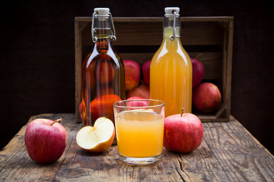 Bottle and glass of apple juice, cloudy and clear, red apples on wood