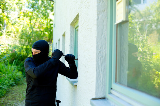 Burglar with crowbar breaking window