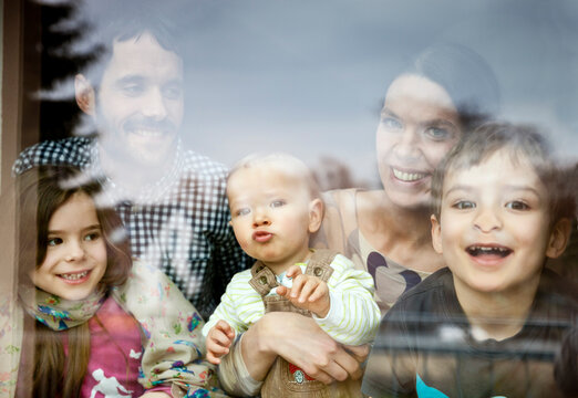 Happy family of five looking through window pane