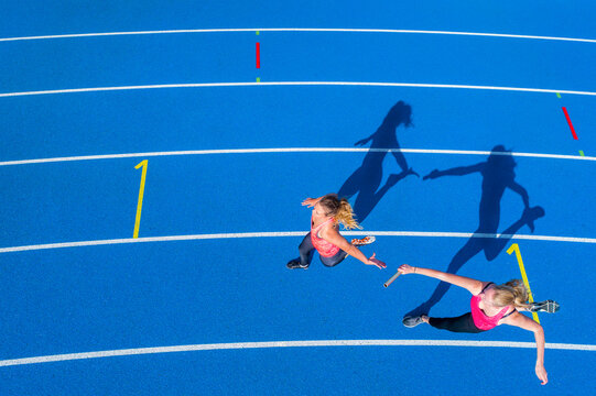 Top view of two female runners passing the baton on tartan track