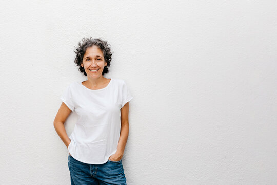 Smiling mature woman with short hair standing against white wall