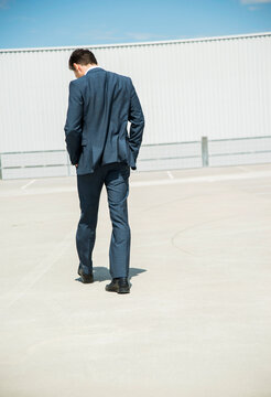 Business man walking on parking level, back view
