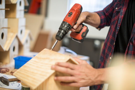 Man working with electric drill on birdhouse in workshop