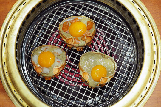 King crab shell loaded with kani miso topped with salmon, shrimp and egg yolk on the iron grate over electric gas stove.