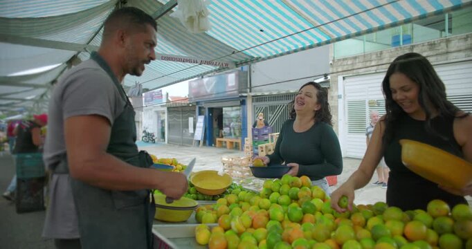 Hispanic street vendor chatting with customers at outdoor market while preparing citrus fruit conveying friendliness trust and everyday local food commerce