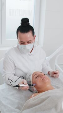 Peeling, woman health care, skin regeneration, dermapen microneedling, dermastamp. Beautician cosmetologist doing procedure fractional microneedle mesotherapy clinic facial rejuvenation. Vertical