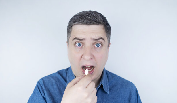 Man suffering from phagophobia struggling to swallow pill. Caucasian male looking anxious and scared before taking medication, experiencing fear of choking or swallowing difficulties.