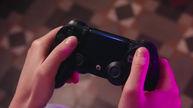 Close-up of a hand holding a game controller, actively playing video games. A fun and engaging leisure moment, showing entertainment and enjoyment at home. High quality 4k footage