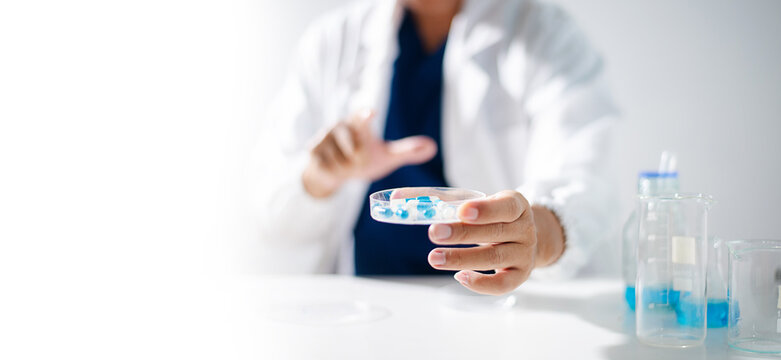 A professional scientist in a lab coat inspecting blue and white medical capsules on a petri dish. Concept of pharmaceutical research, health care development