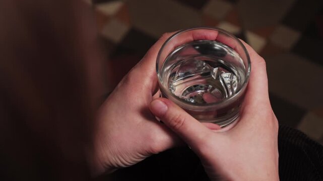 Over the shoulder view of a person holding a glass of water during a calm consultation setting, possibly in a psychologist or doctor office. Concept of represents mental health care, patient