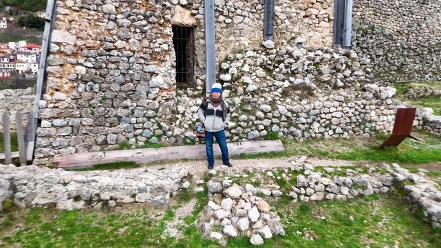 Aerial perspective pulling away and rising from DIY Destinations host Charles Huang to reveal the historic stone walls of Kruje Castle and the surrounding Albanian landscape
