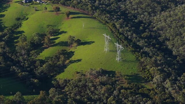 Beautiful drone video gliding over Mt Lofty&rsquo;s rolling green hills near Melbourne, showing tall powerlines cutting through dense forest under soft, natural daylight. Pristine landscape, no people.
