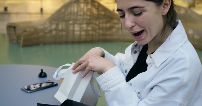 Joyful gift unveiling. Woman excitedly opens small present. Woman happily reveals tiny gift with delight. Woman experiences pure happiness as she unveils tiny gift with excitement and smile