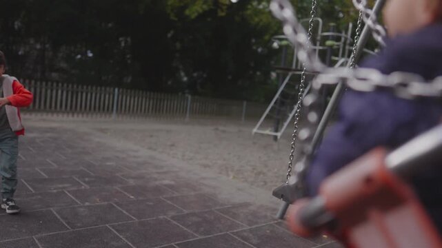 Child playfully pushing toddler on swing in gentle motion creating joyful playground moment showing sibling interaction balance movement and natural outdoor energy
