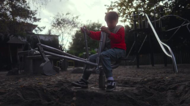 Child sitting on metal sand digger concentrating on moving arm through sand creating dynamic playground moment showing control coordination physical effort and imaginative outdoor play in park setting