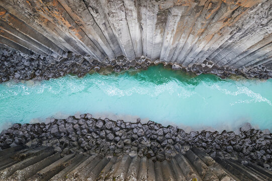 Aerial view of the turquoise glacial river flowing through the towering basalt columns of Studlagil Canyon in Eiriksstadhir, Mulathing, Iceland.